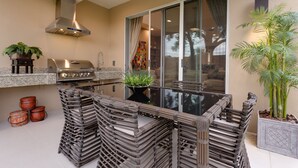 An outdoor kitchen with a grill, a sink, and a dining area with a glass table and chairs. - 4 B/R Villa, Free Parking & Free Wi-Fi, Near Disney Family Friendly (Kissimmee)