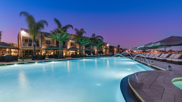 A swimming pool with lounge chairs and umbrellas, surrounded by palm trees and a building with multiple balconies. - 4 B/R Villa, Free Parking & Free Wi-Fi, Near Disney Family Friendly (Kissimmee)