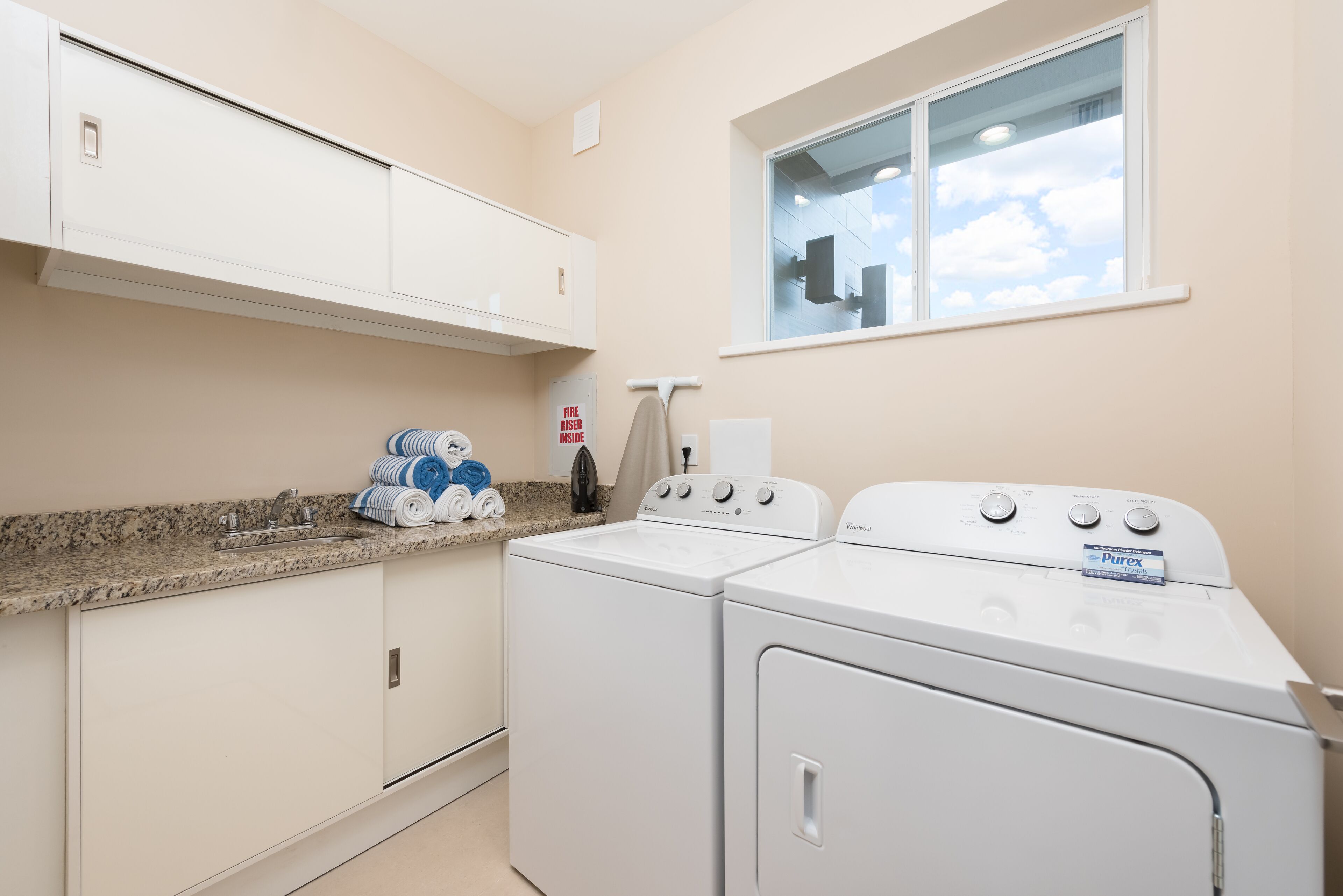 A laundry room with a washer and dryer, a countertop with towels, and a window with a view of the sky.