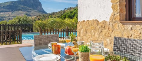 A table set for breakfast with a mountain view, a pool, and a stone wall.