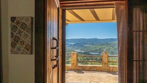 An open wooden door leading to a balcony with a stone floor, a view of a lake, and a mountainous landscape. - Vistahermosa del Gastor by Ruralidays (Cádiz)
