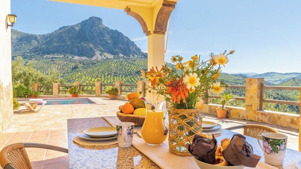 A terrace with a table set for breakfast, a vase of flowers, and a mountain view. - Vistahermosa del Gastor by Ruralidays (Cádiz)