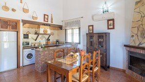 A kitchen with a central island, a dining table with chairs, a washing machine, a stove, and a fireplace. - Vistahermosa del Gastor by Ruralidays (Cádiz)