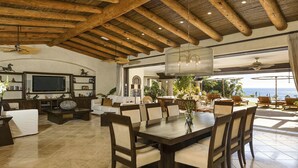 A spacious living area with a large dining table, comfortable seating, a TV, and a view of the ocean. - Poolside Bliss Awaits, Cabo San Lucas Villa 1006 (Cabo San Lucas)