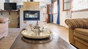 Un salon comprenant une table basse sur laquelle se trouve un plateau avec une théière et des tasses, une cheminée, un canapé et un téléviseur posé sur un meuble.