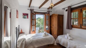 Une chambre avec deux lits, une armoire en bois et un balcon donnant sur un paysage verdoyant.