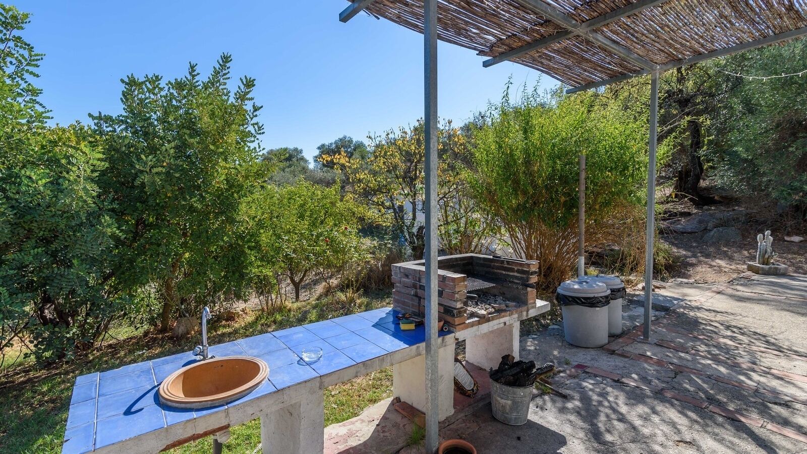 Un área de cocina exterior con una parrilla empotrada, un lavamanos y un cubo de basura.