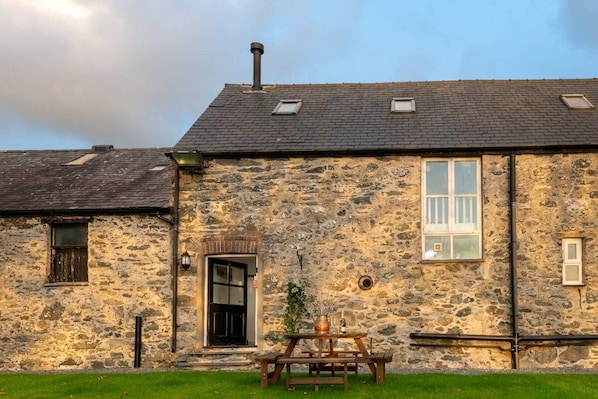 A stone building with a pitched roof, a front door, and a small table with a plant.