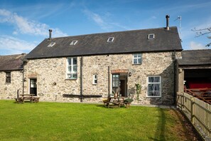 A stone building with a sloped roof, a wooden bench, and a picnic table in the foreground. - Hill Top: 5 bedroom Anglesey holiday barn conversion (Caergeiliog)