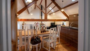 A dining area with a wooden ceiling, white chairs, and a table set for four. - Bryn Lon Mawr: 5-Bed Barn Conversion in Caergeiliog | Managed by Anglesey Holiday Lettings (Caergeiliog)