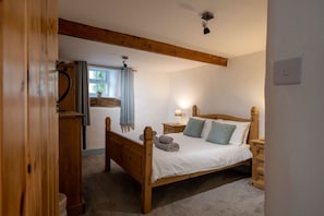 A bedroom with a wooden bed, a nightstand, a lamp, and a window with curtains.