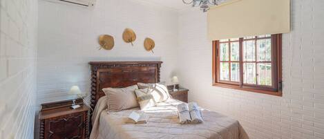 A bedroom with a wooden bed, a nightstand, a bedside lamp, a window with a view, and a chandelier.