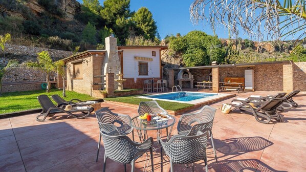 Un espace piscine avec des chaises longues, une table avec des boissons et un mur en pierre.