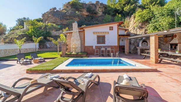 Ein Poolbereich mit Liegestühlen, ein kleines Gebäude mit einem Steinofen und eine Terrasse mit Tischen und Stühlen.