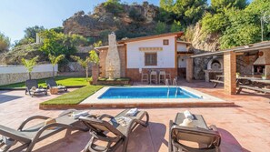 Un espace piscine avec des chaises longues, un petit bâtiment doté d’une cheminée en pierre et une terrasse avec des tables et des chaises.