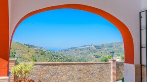 A view through an archway with a stone wall and a potted plant, overlooking a hilly landscape with a clear sky.