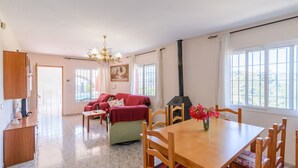 A spacious living area with a sofa set, a dining table with chairs, a chandelier, and a large window with a view.