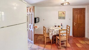 A dining area with a table set for two, a television on the wall, and a wooden door. - Casa Madrona Periana by Ruralidays (Málaga)