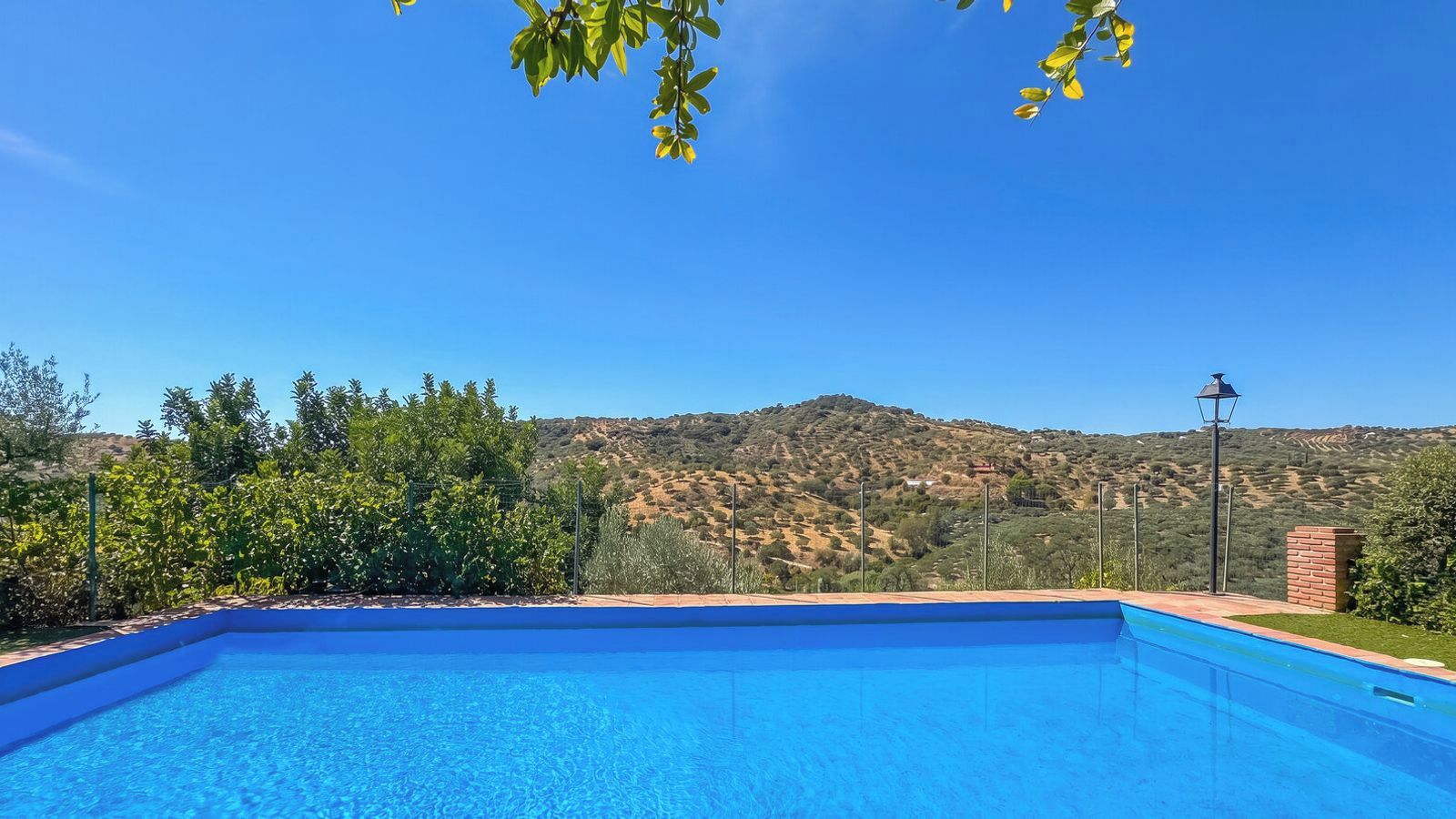 A clear blue swimming pool with a view of a hilly landscape in the background.