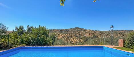 A clear blue swimming pool with a view of a hilly landscape in the background.
