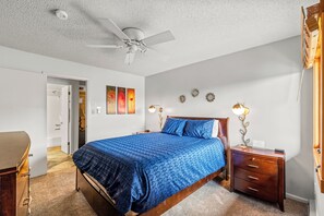 Une chambre à coucher avec un lit, des tables de chevet, un ventilateur de plafond et des œuvres d’art accrochées au mur.