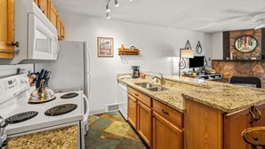 A kitchen with a stove, sink, wooden cabinets, granite countertop, and a stone fireplace. - Ski Inn 1-Bedroom Retreat with Hot Tub Access! (Steamboat Springs)