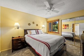 A bedroom with a bed, nightstand, lamp, ceiling fan, and a window with a view.