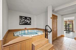 Un jacuzzi en un rincón con escalones de madera y una puerta que da a un espacio al aire libre.