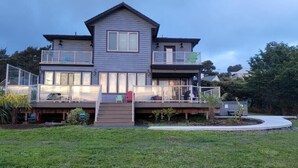 A two-story house with a balcony on the upper floor, a covered deck, and a small garden area. - Beautiful Home with Ocean View, Large Yard, and Hot Tub  (Lincoln City)