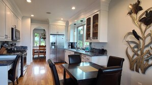 A modern kitchen with white cabinetry, a granite countertop, and a dining area with a table and chairs. - Beautiful Home with Ocean View, Large Yard, and Hot Tub  (Lincoln City)