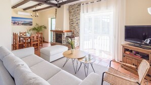 A living room with a sofa, a dining table with chairs, a fireplace, a television, and a balcony with a view. - Cortijo La Jirafa Torrox by Ruralidays (Málaga)