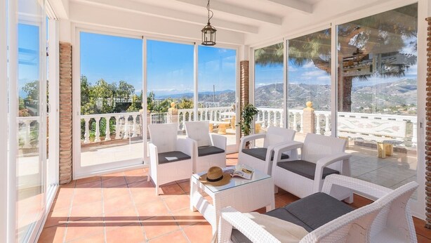A sunlit patio with white wicker furniture, a glass table, and a view of a mountainous landscape. - Cortijo La Jirafa Torrox by Ruralidays (Málaga)