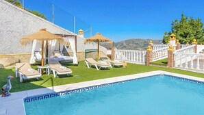 A pool area with lounge chairs, a small statue, and a thatched-roof structure. - Cortijo La Jirafa Torrox by Ruralidays (Málaga)