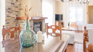 A dining area with a wooden table, chairs, a vase with dried wheat stalks, and a stone wall in the background. - Cortijo La Jirafa Torrox by Ruralidays (Málaga)