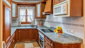 A compact kitchen with wooden cabinets, a microwave, a sink, and a fruit bowl on the counter. - Villa Mi Paraíso Torrox by Ruralidays (Málaga)