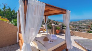 A private balcony with a wooden canopy bed, a small table with a bottle and glasses, a potted plant, and a view of the coastline. - Villa Mi Paraíso Torrox by Ruralidays (Málaga)
