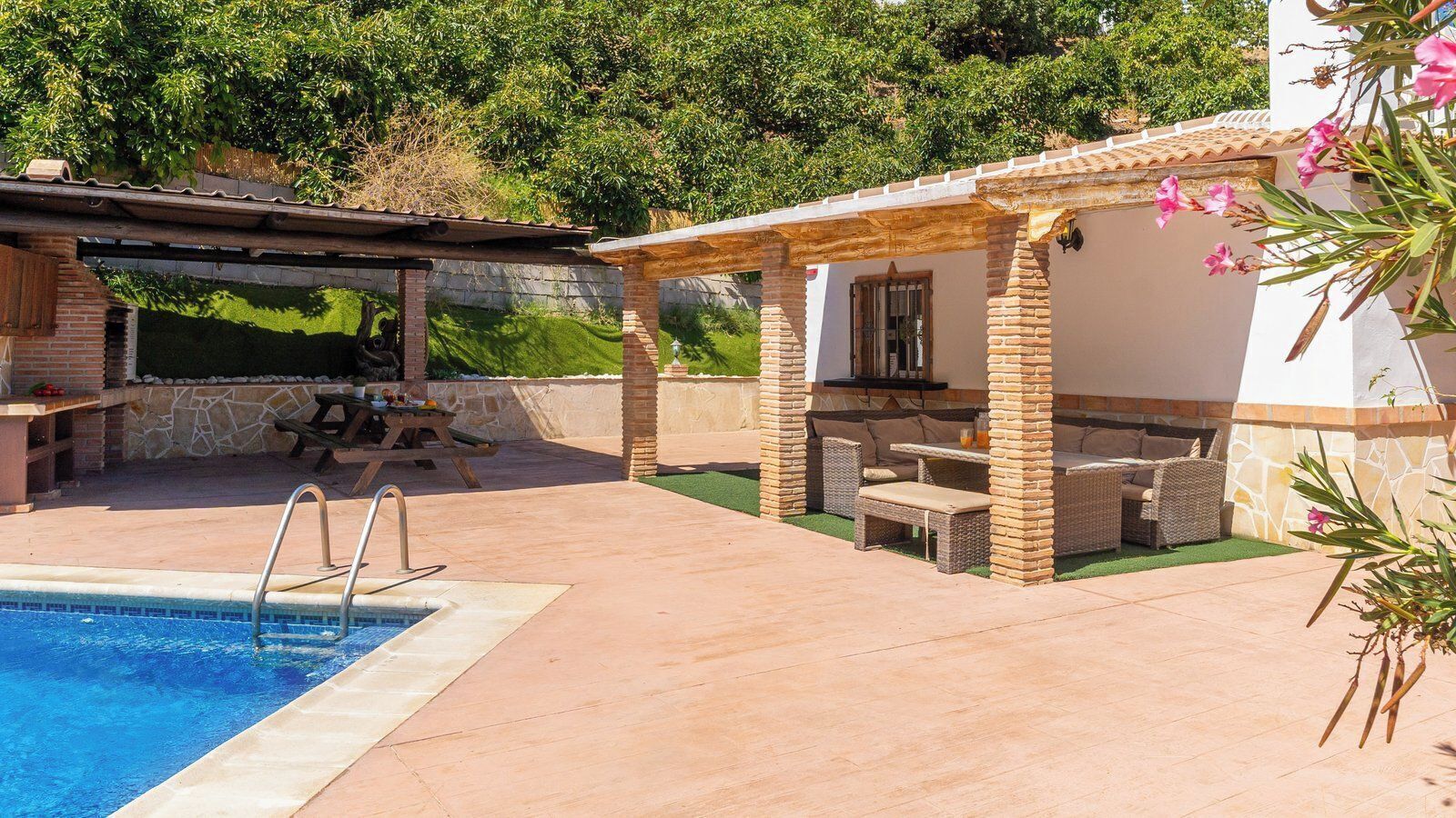 A pool with a built-in ladder, a covered patio area with outdoor furniture, and a stone wall in the background.