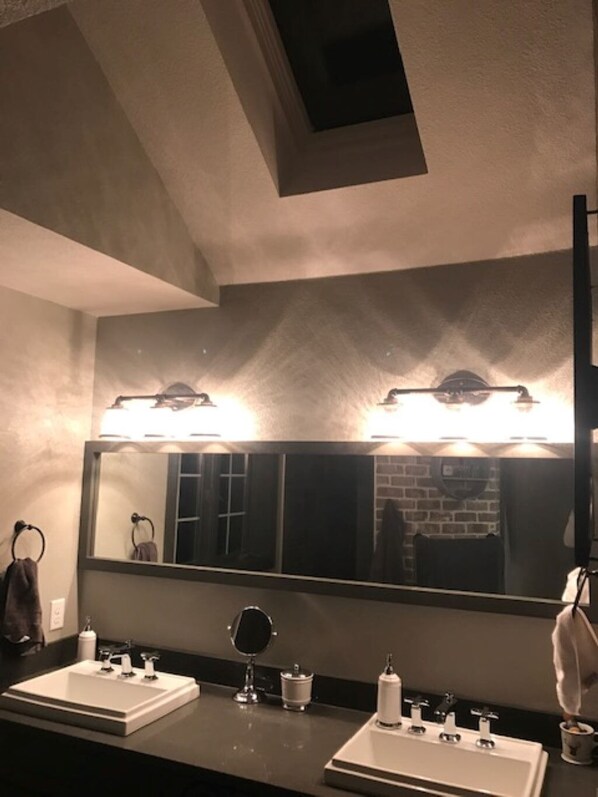 Un baño con dos lavamanos, un espejo grande e iluminación en el techo.