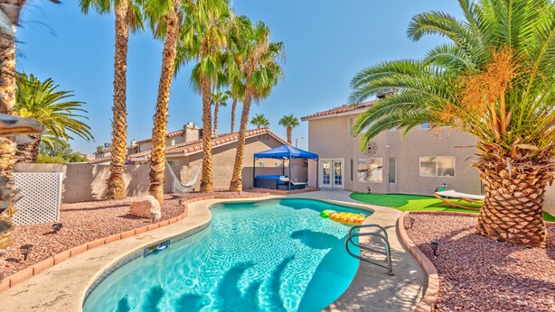 A swimming pool surrounded by palm trees, a covered seating area, and a building with a tiled roof. - Modern & Cozy | 13min to Strip, ♛Royal Beds, Pool (Henderson)