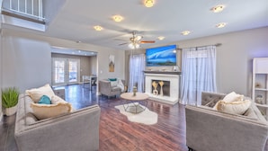 A spacious living room with a fireplace, a ceiling fan, and a large TV. - Modern & Cozy | 13min to Strip, ♛Royal Beds, Pool (Henderson)
