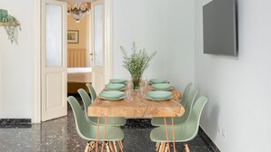 A dining area with a wooden table set for six, surrounded by green chairs, a vase with greenery, and a chandelier. - The dreamer house design (Roma)