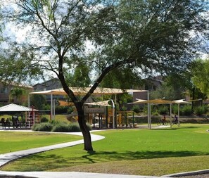 Stroll through a serene park with a majestic tree, a grassy area, and a path leading to a recreational facility with a climbing wall and seating area.