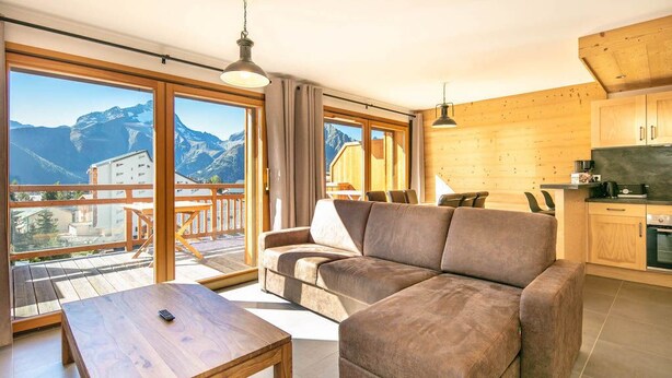 Una sala de estar moderna con un sofá grande, una mesa de centro de madera y un balcón con vistas a las montañas.