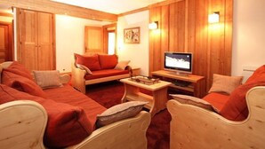 A cozy room with wooden walls and furniture, including a sofa, chairs, and a TV.