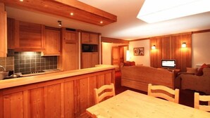 A kitchen with wooden cabinets, a dining table, and a TV in the living area.