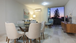 A modern dining area with a glass table and four chairs, a wooden sideboard, and a view of a tree through a large window. - Apartment with GREAT LOCATION, 1 block from the boardwalk (La Paz)