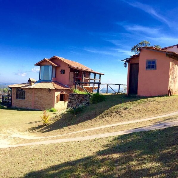 A two-story house with a balcony, a stone foundation, and a dirt path leading to the entrance.