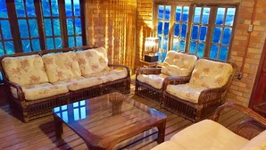 A cozy seating area with a sofa, two armchairs, and a coffee table, all made of wicker, with a view of the sea through large windows. - White Mountain (Conceição da Ibitipoca)