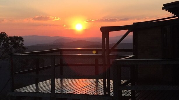 A wooden deck overlooking a sunset with distant mountains. - White Mountain (Conceição da Ibitipoca)