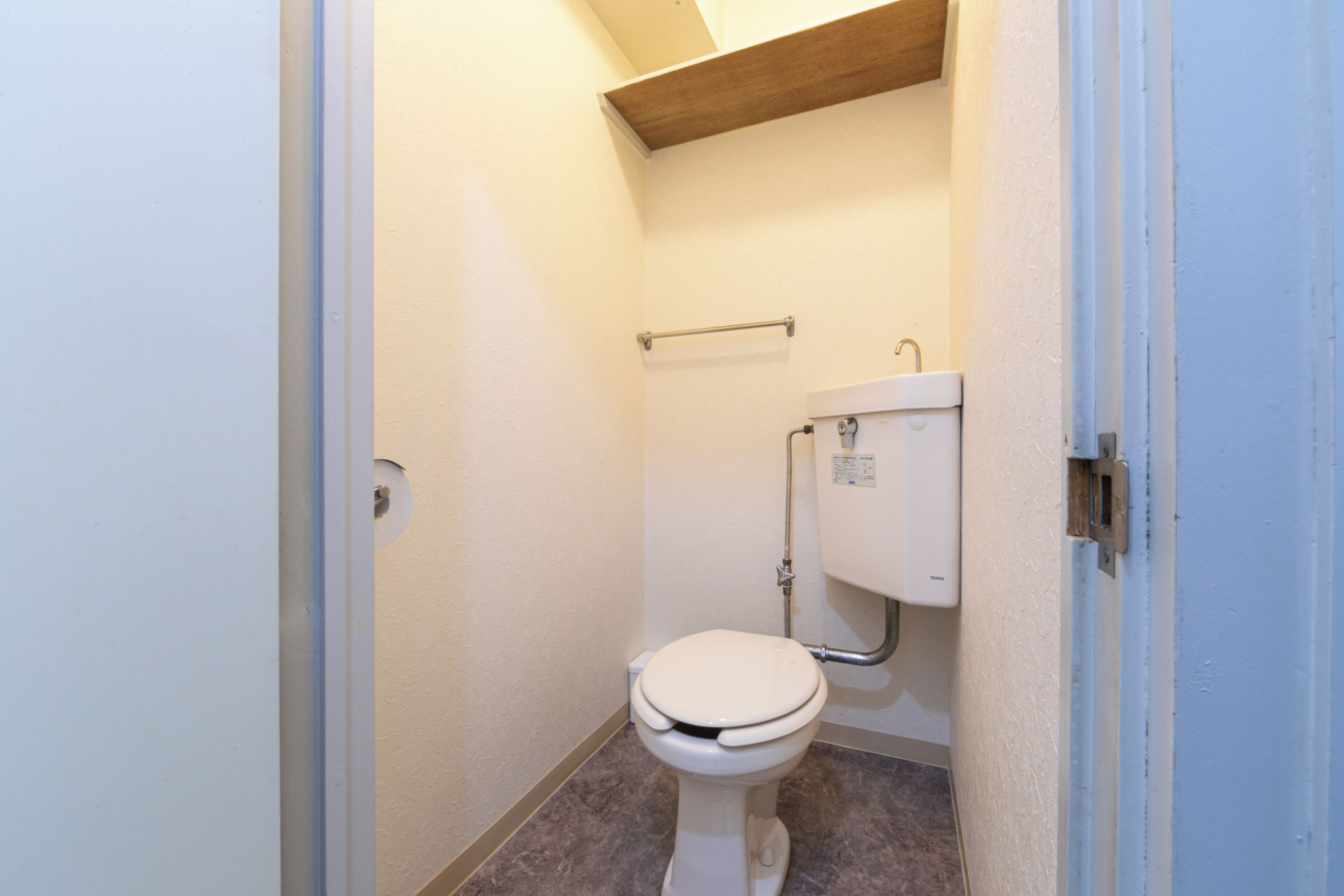 A small, clean bathroom with a toilet, a towel rack, and a wooden ceiling.